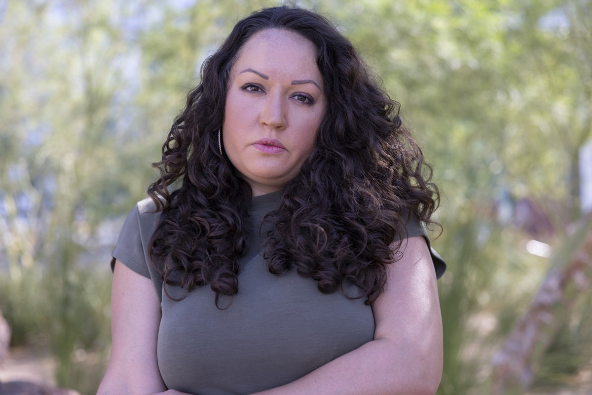 kobieta w średnim wieku z burzą ciemnych loków stoi na dworze i patrzy przed siebie zdegustowanym wzrokiem