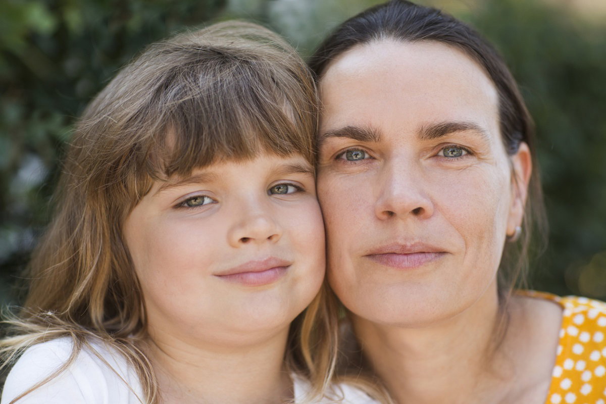matka z córką przytulają się głowami i lekko się uśmiechają, ale matka ma poważne oczy