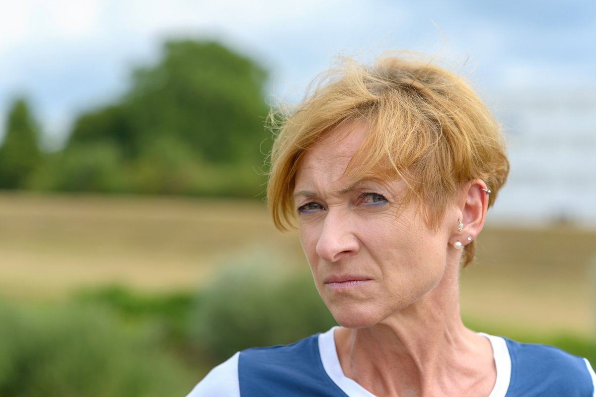 kobieta seniorka z krótkimi włosami stoi na zewnątrz i patrzy podejrzliwym wzrokiem