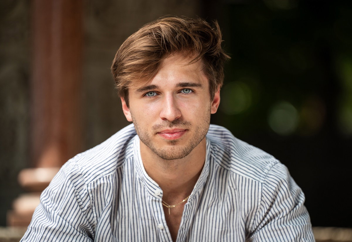 młody mężczyzna w koszuli w paski i z rozwichrzoną czupryną patrzy przed siebie zadowolonym wzrokiem