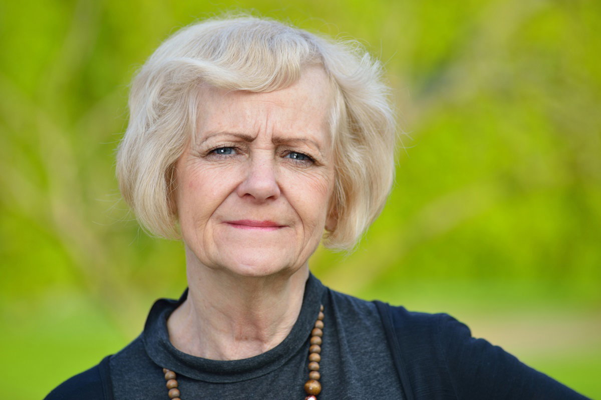 kobieta w dojrzałym wieku i w czarnym ubraniu i z koralami patrzy ze łzami w oczach przed siebie