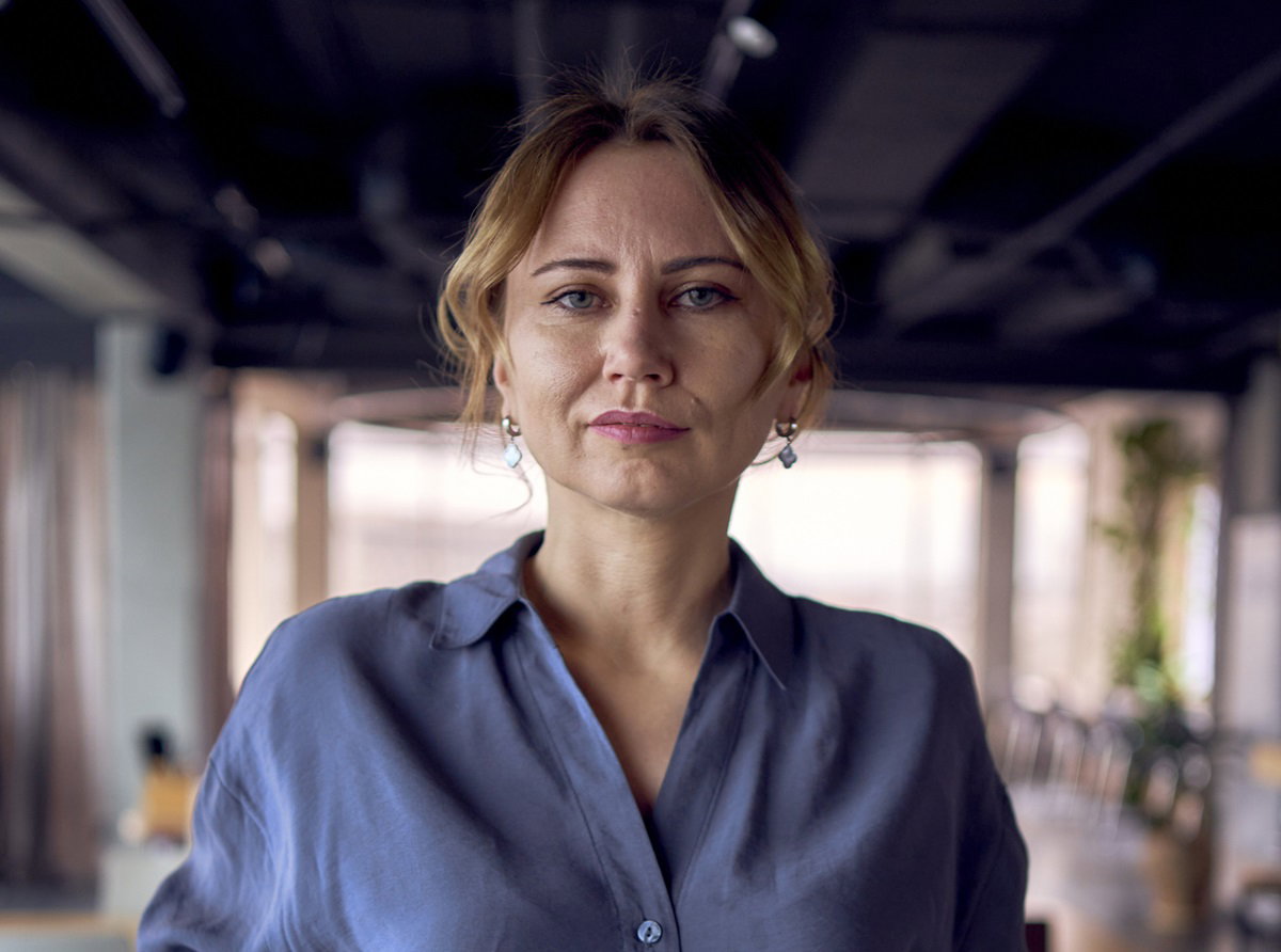 młoda kobieta ze spiętymi włosami w niebieskiej koszuli stoi w biurze i patrzy surowym wzrokiem