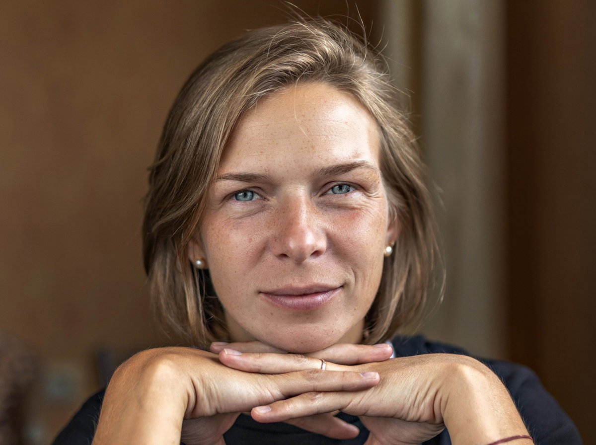 młoda kobieta z rękami pod brodą i włosami ciemny blond lekko się uśmiecha patrząc przed siebie