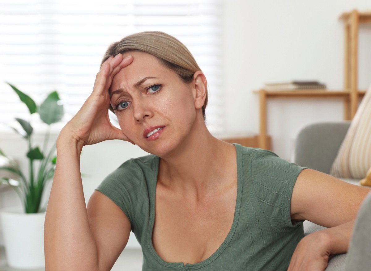 kobieta w średnim wieku blondynka siedzi na ziemi w salonie i trzyma się za głowę zmartwiona