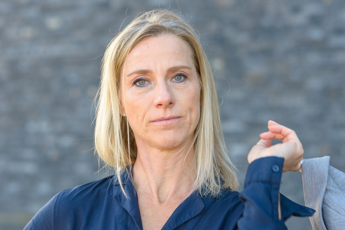 kobieta w średnim wieku w granatowej koszuli i z długimi blond włosami patrzy ze zdegustowaną miną