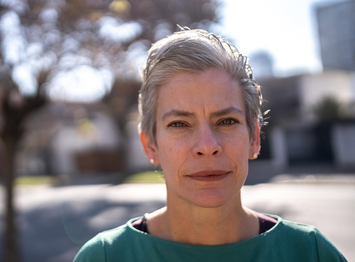 kobieta w dojrzałym wieku z krótkimi siwymi włosami stoi na zewnątrz i patrzy surowym wzrokiem