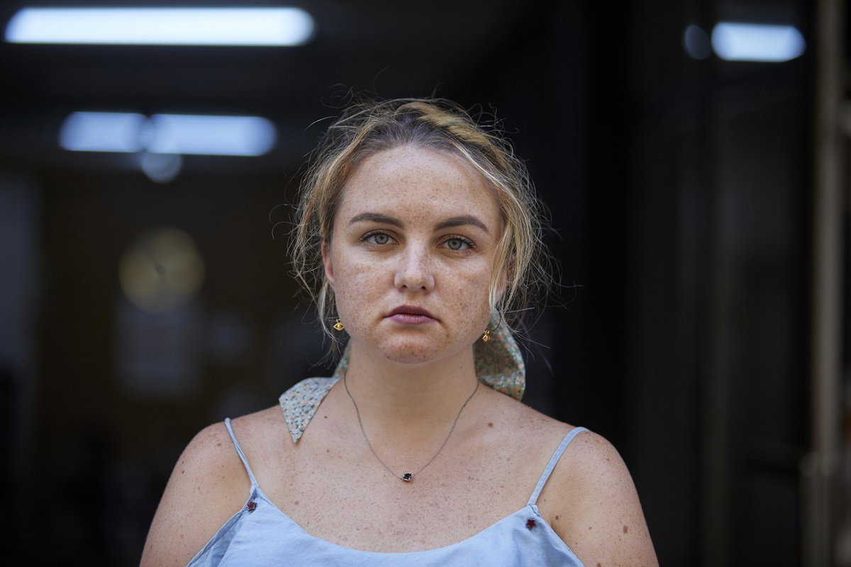 młoda dziewczyna z piegami i jasnymi włosami spiętymi do tyłu w letniej sukience stoi ze smutną i poważną miną