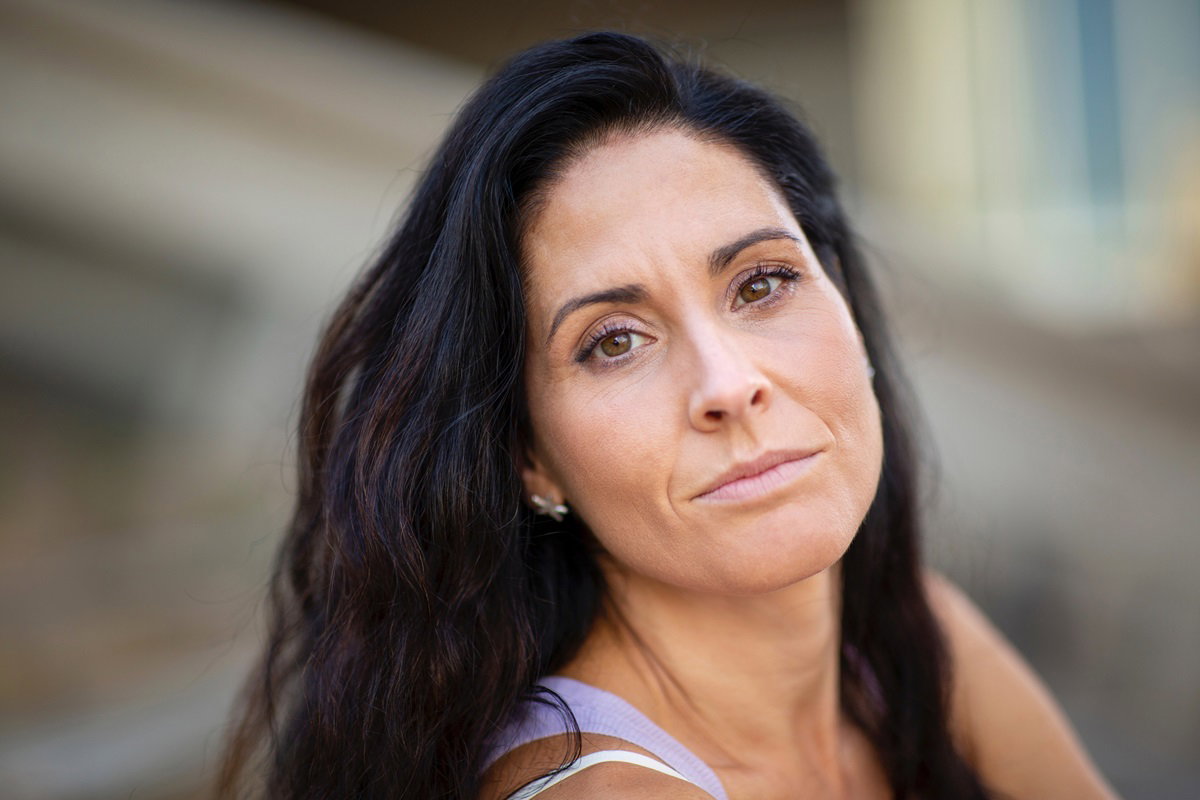 młoda kobieta z długimi ciemnymi włosami patrzy zamyślona przed siebie