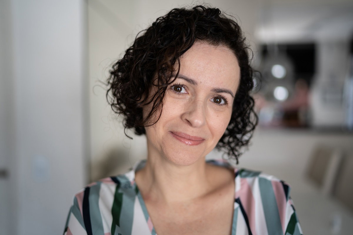 kobieta w średnim wieku około 40stki z ciemnymi kręconymi włosami na pazia stoi w salonie i patrzy lekko uśmiechnięta przed siebie