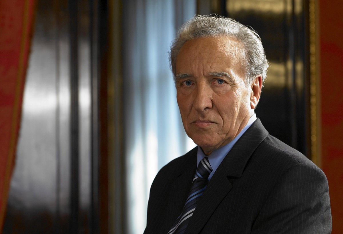 mężczyzna w wieku senioralny z siwymi włosami i w garniturze patrzy przed siebie zgorzkniały wzrokiem