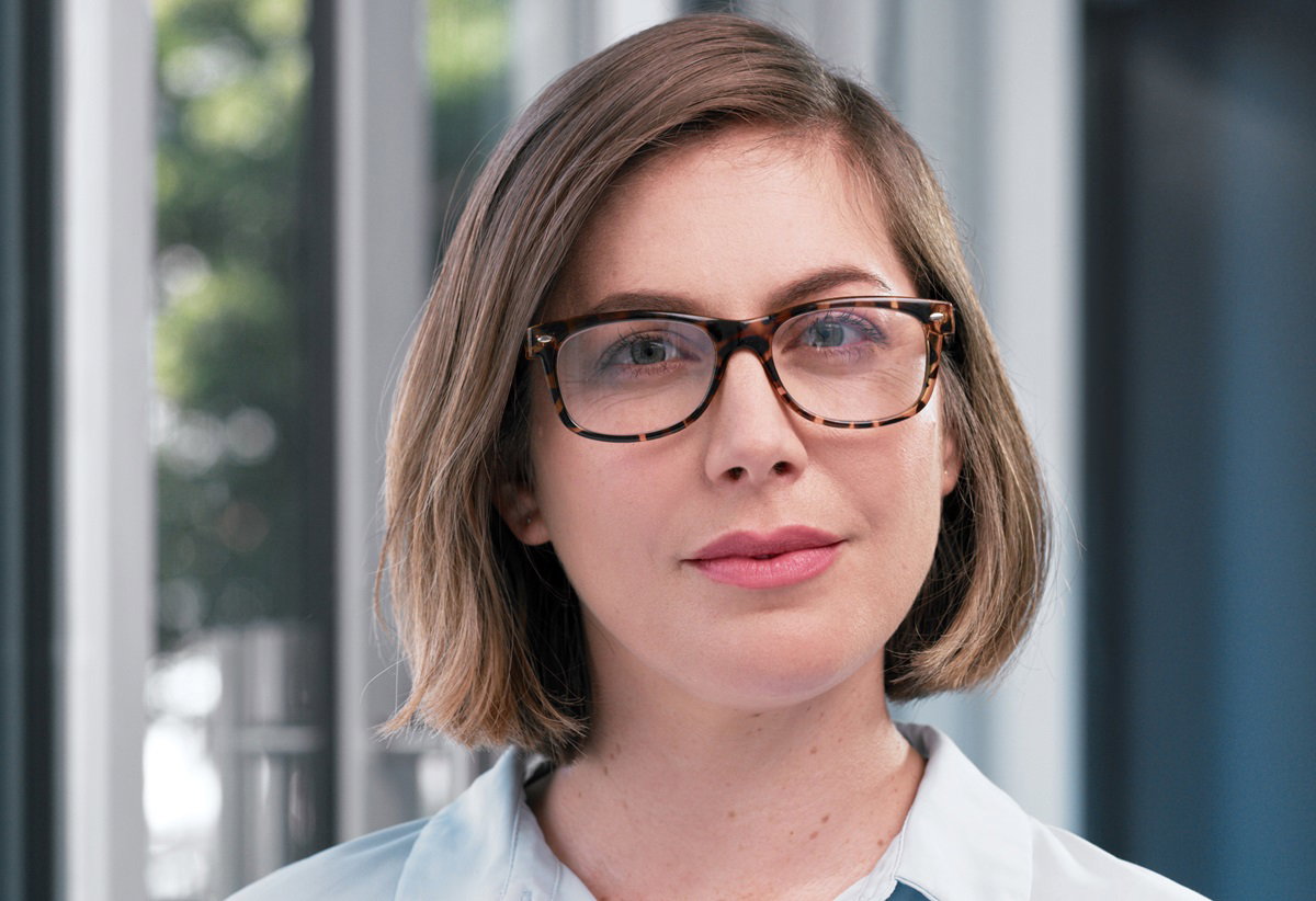 młoda kobieta w okularach z fryzurą na pazia stoi i patrzy przed siebie poważnym wzrokiem