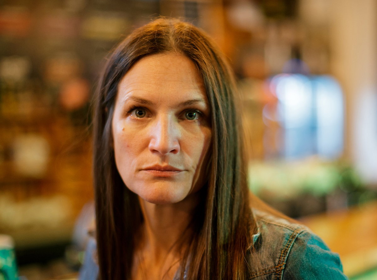 kobieta w średnim wieku z długimi włosami i w jeansowej kurtce patrzy przed siebie przerażonym wzrokiem