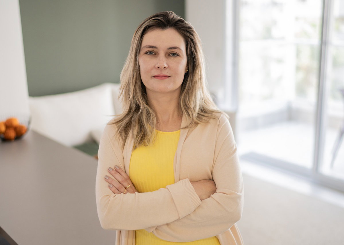 kobieta w średnim wieku z jasnymi włosami stoi w kuchni z założonymi rękami i poważną miną