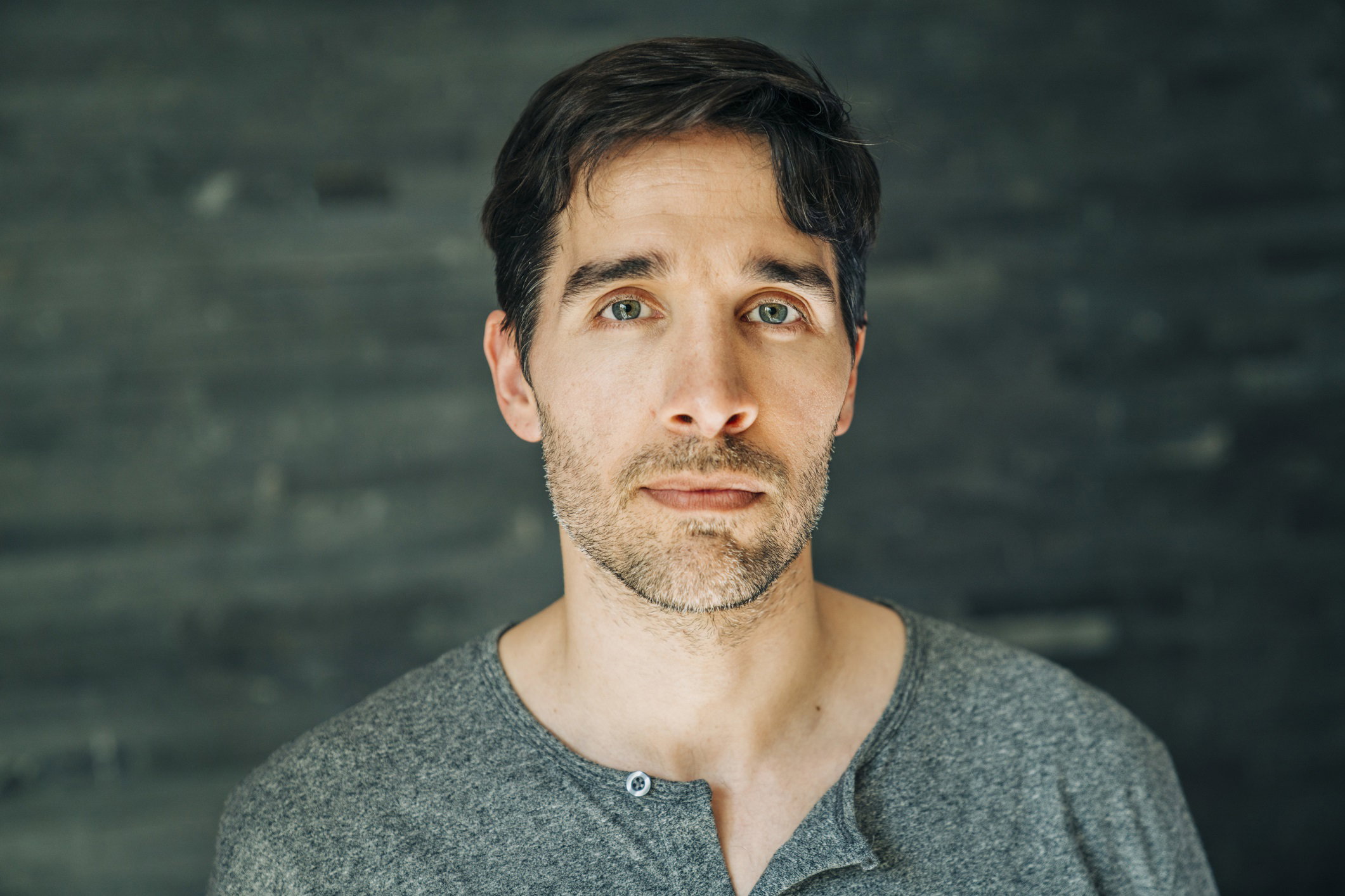 młody mężczyzna z zarostem i w szarej bluzce stoi i patrzy smutnym wzrokiem przed siebie