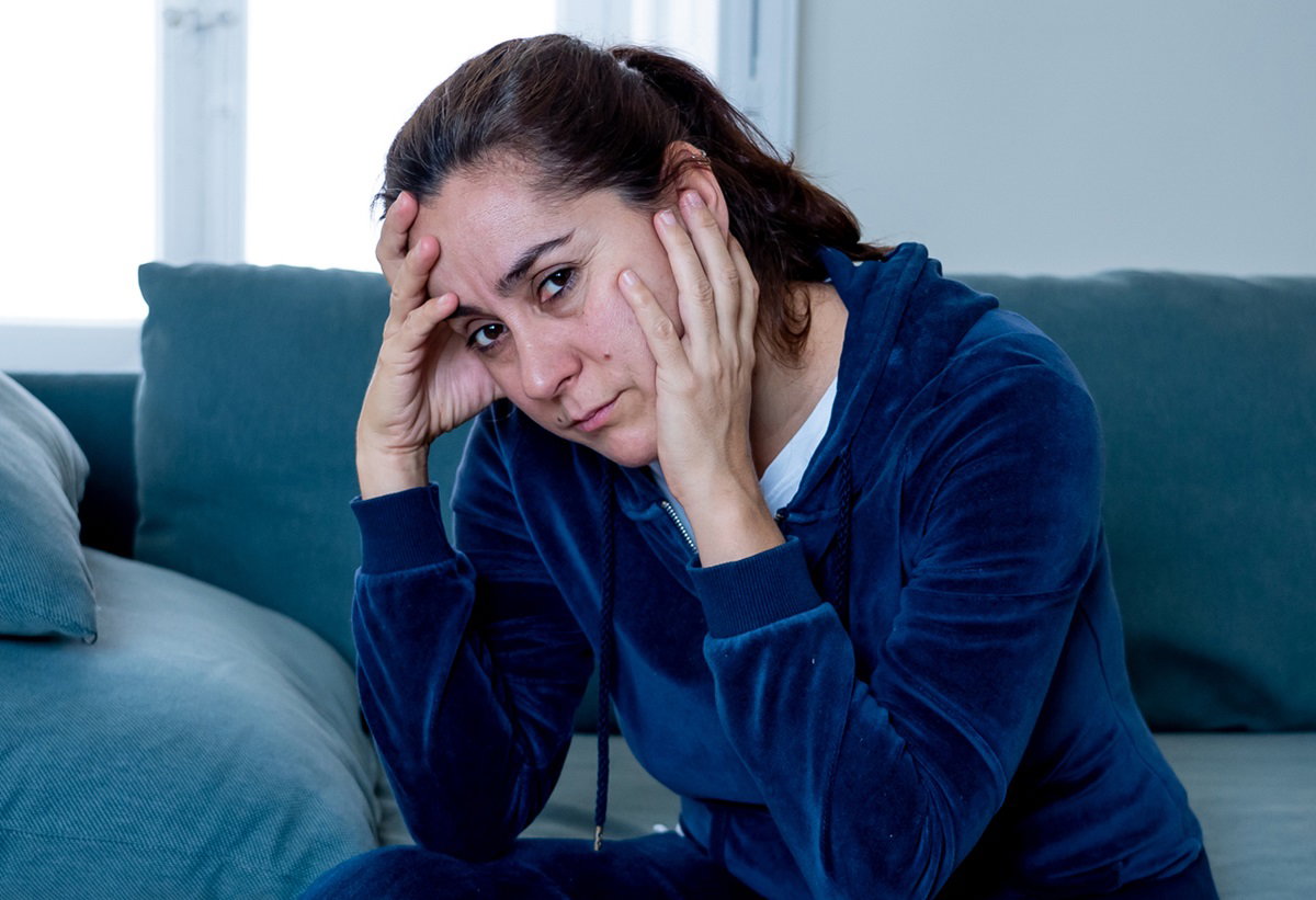 kobieta z ciemnymi włosami zebranymi w kucyk siedzi na kanapie w salonie w welurowym dresie i jest w rozpaczy