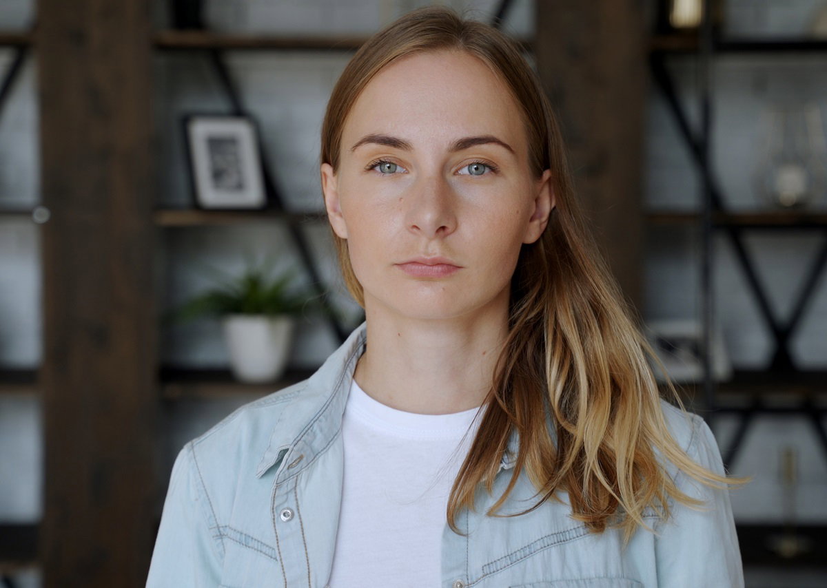 młoda dziewczyna z długimi włosami ciemny blond stoi w salonie i ma poważną minę
