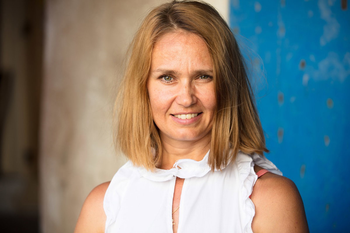 młoda kobieta z włosami ciemny blond i w białej bluzce stoi z lekkim zawadiackim uśmiechem