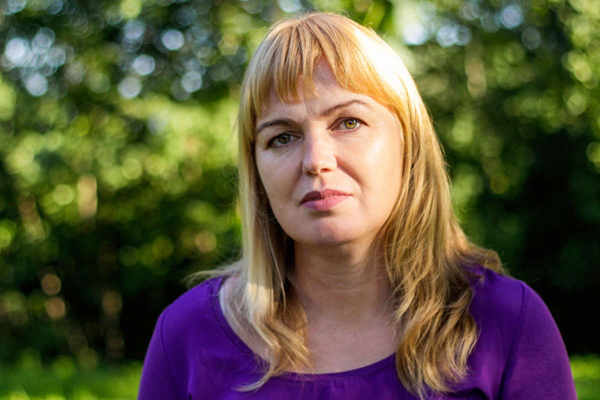 kobieta w średnim wieku około 40+ z blond włosami z grzywką i w fioletowej bluzce siedzi na ławce w parku i jest smutna