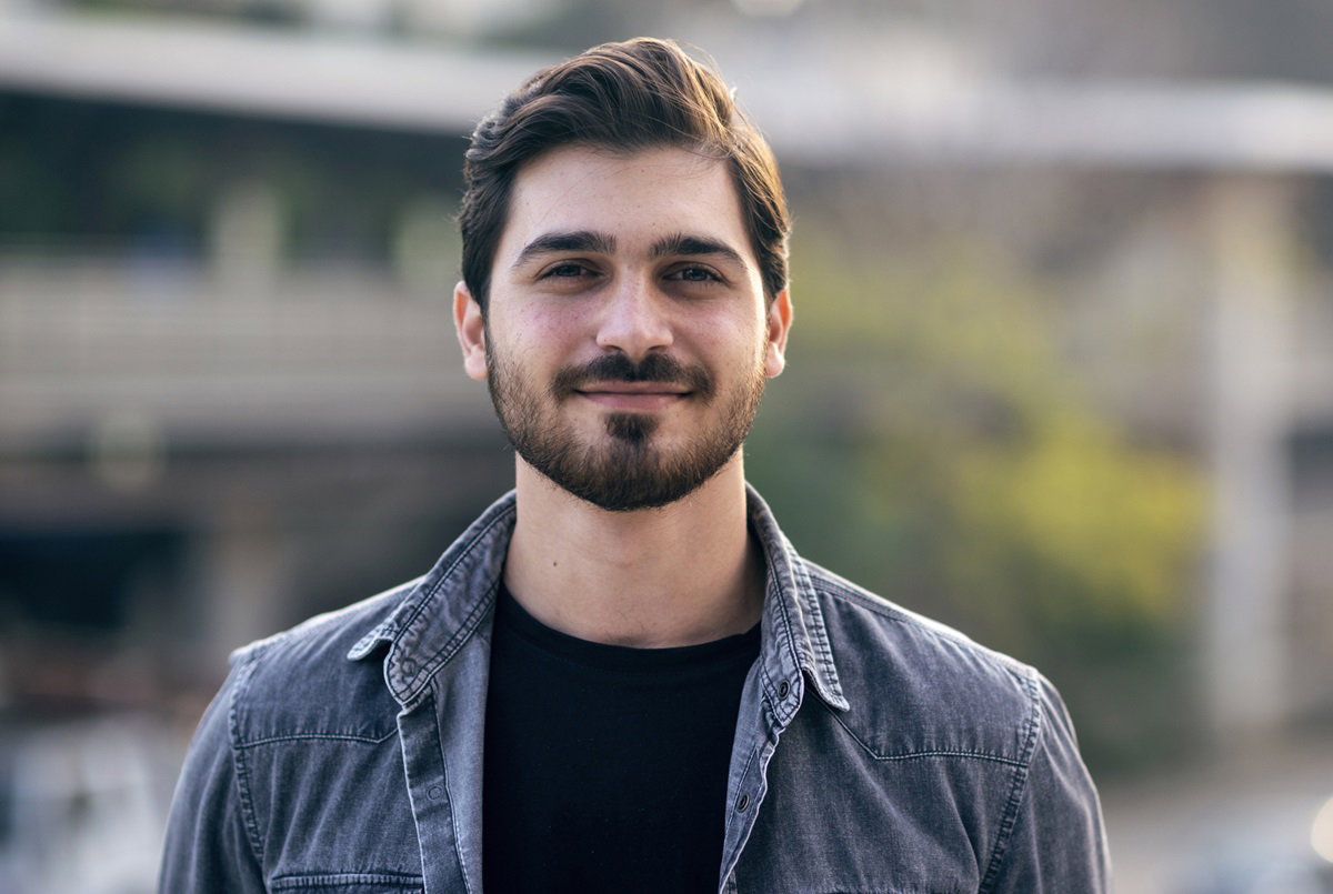 młody mężczyzna w wieku około 30 lat z brodą i wąsami w jeansowej koszuli stoi na ulicy i uśmiecha się zadowolony