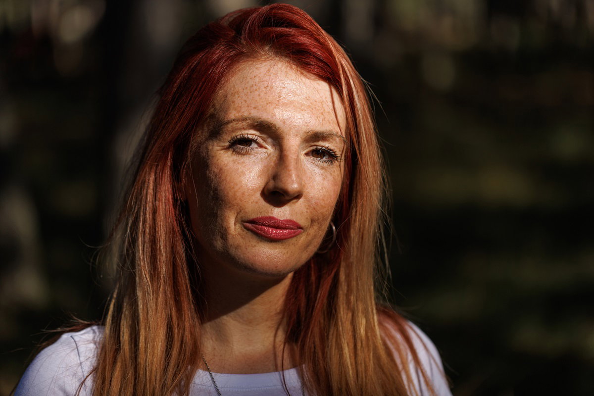 młoda kobieta z rudymi włosami i piegami stoi na zewnątrz i patrzy zgorzkniałym spojrzeniem przed siebie