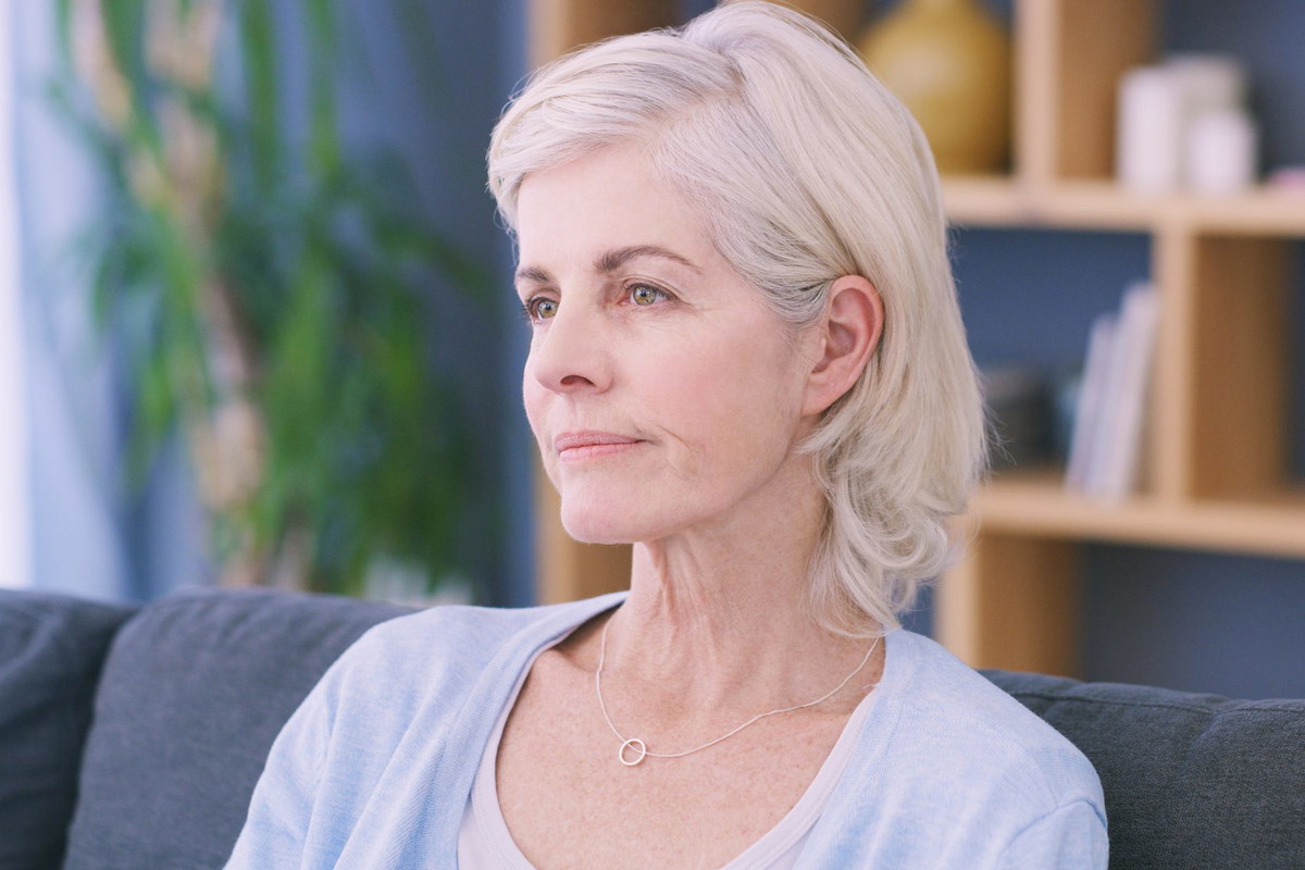 Shot of an older woman looking sad while lost in thought on the sofa at home