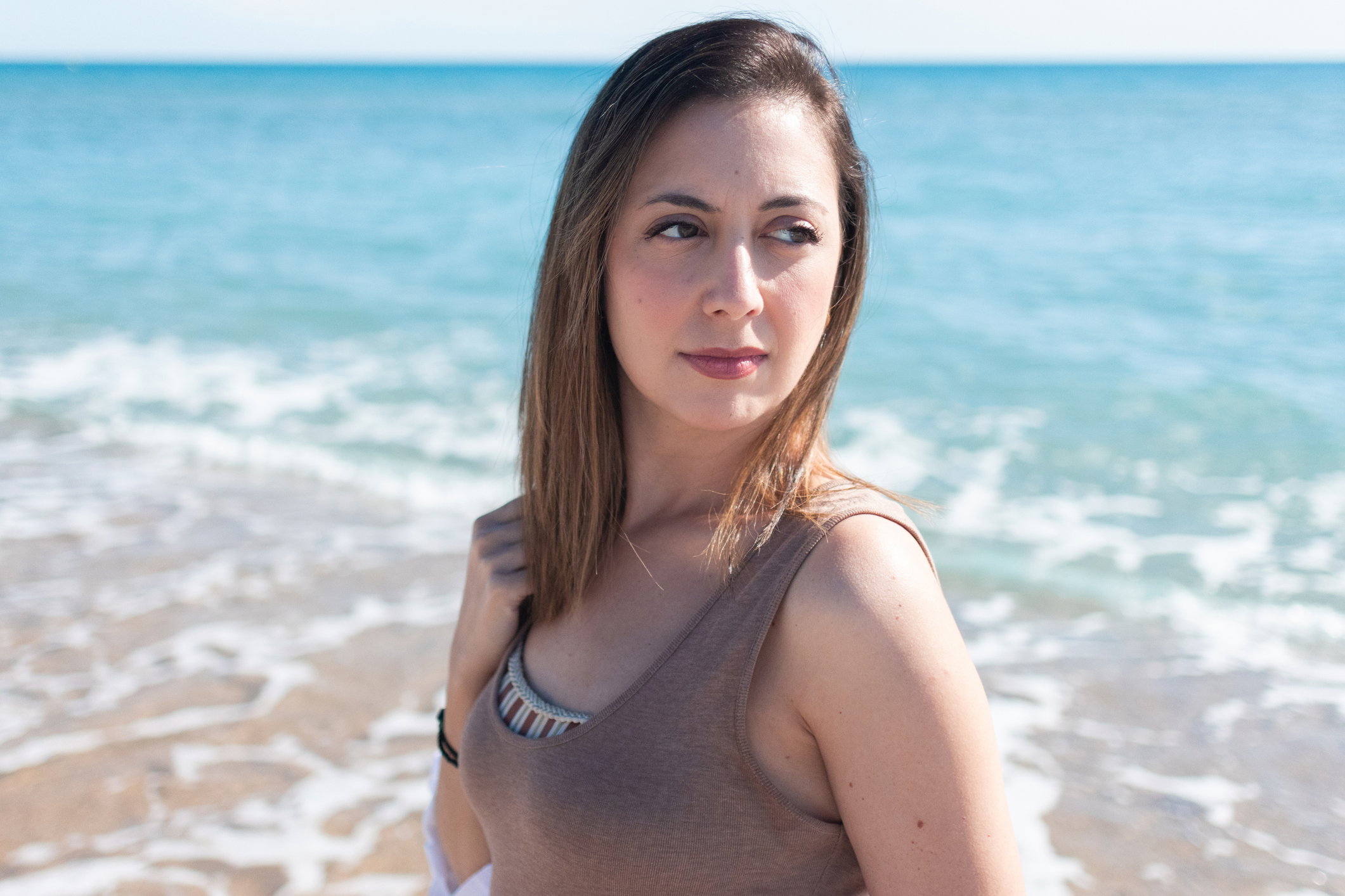 beautiful Caucasian adult woman sad and serious thinking and with negativity in her eyes and facial expression in front of the sea at the beach