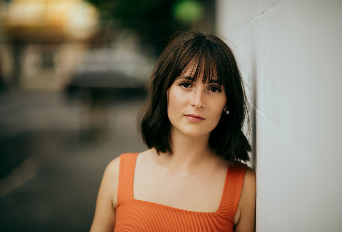 młoda dziewczyna w wieku około 20 lat w czerwonej sukience z czarnymi włosami stoi zamyślona na ulicy