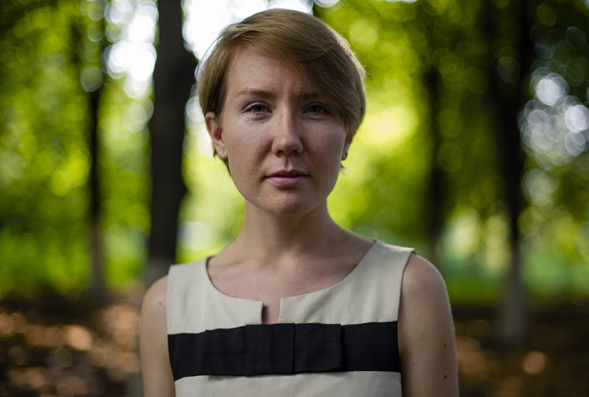 młoda kobieta w wieku około 35 lat z krótkimi włosami stoi na tle lasu i ma poważną trochę zadziorną minę