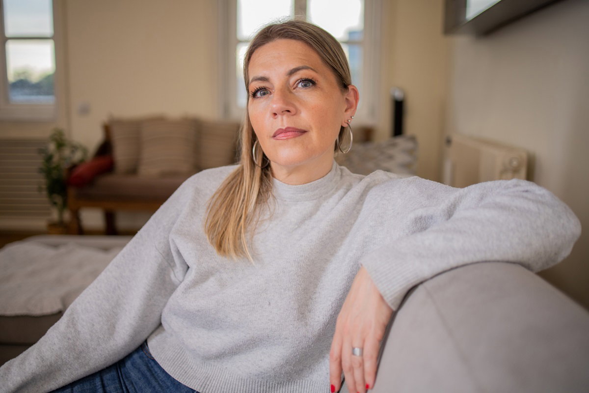kobieta w wieku 40 lat z jasnymi włosami i dużymi kolczykami siedzi na kanapie w salonie z poważną miną