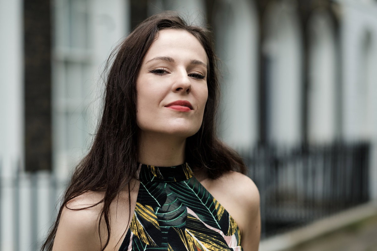 piękna kobieta z długimi włosami w wieku około 30 lat stoi na ulicy w kwiatowej bluzce i ma zadartą głowę wysoko i dumne spojrzenie