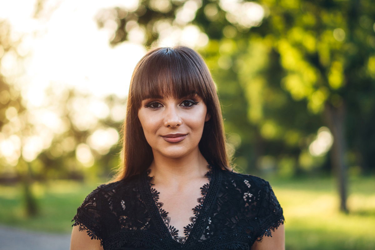 młoda kobieta w wieku około 30 lat w czarnej koronkowej sukience i w pełnym makijażu oraz fryzurze z grzywką stoi na zewnątrz i się uśmiecha