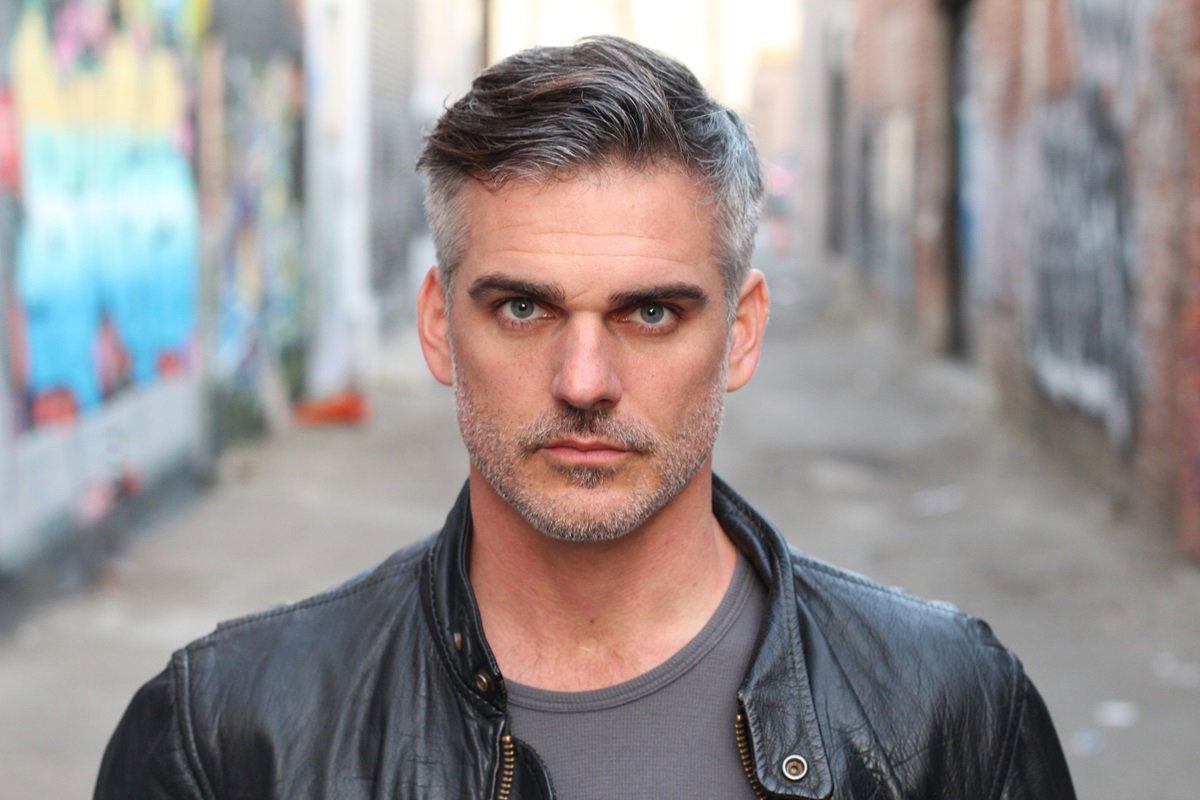 przystojny mężczyzna w dojrzałym wieku z siwymi włosami i zarostem w skórzanej kurtce patrzy groźnym spojrzeniem