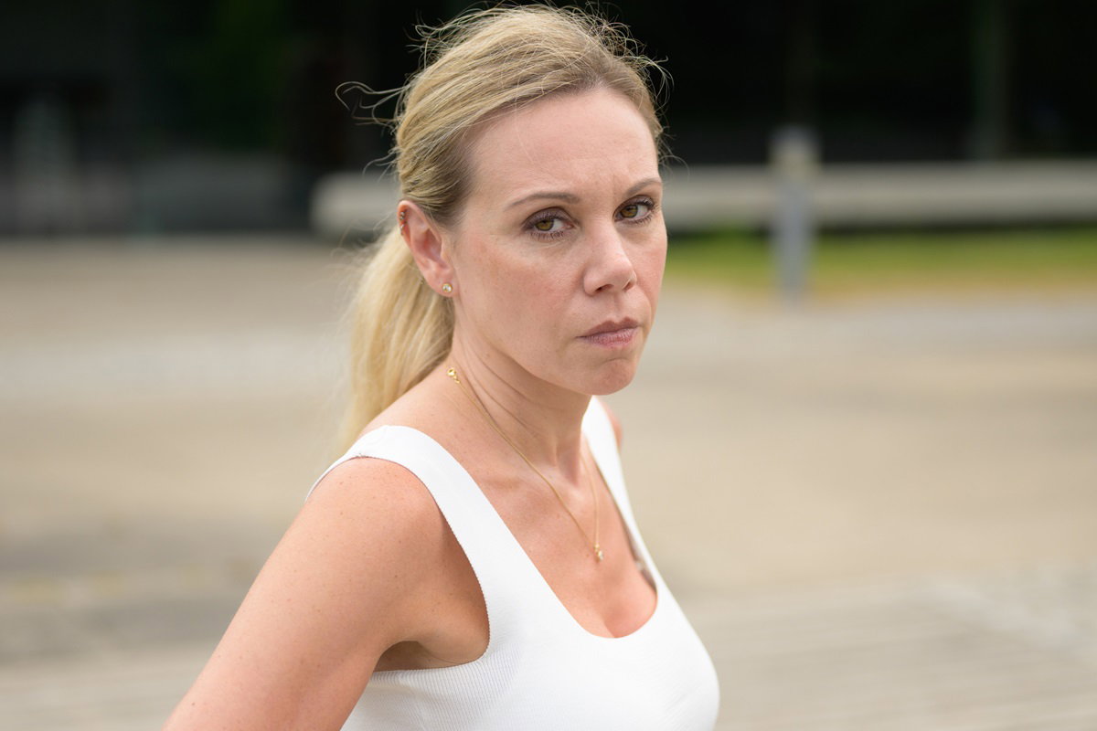 kobieta w wieku około 40 lat blondynka w kucyku w białym topie stoi na zewnątrz ze zdegustowaną miną