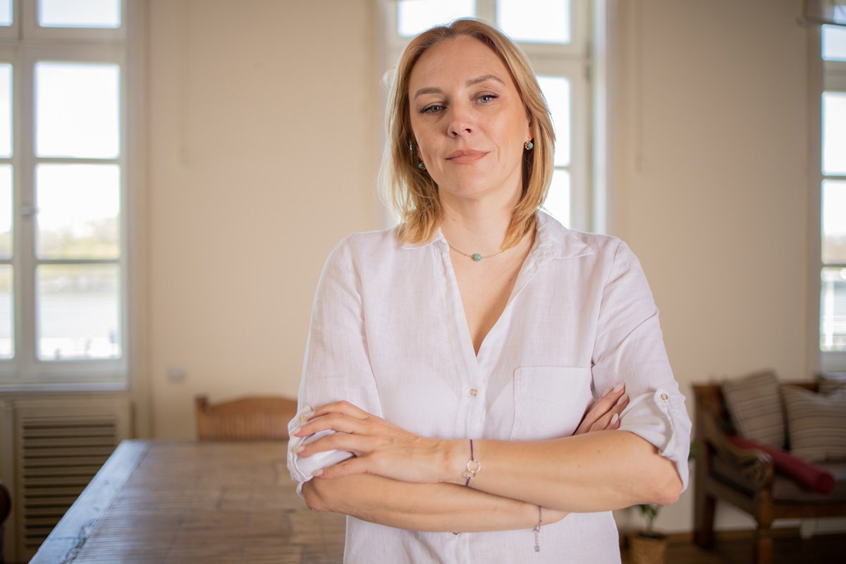 kobieta w średnim wieku około 40 lat w białej koszuli blondynka stoi w salonie z założonymi rękami i poważną miną