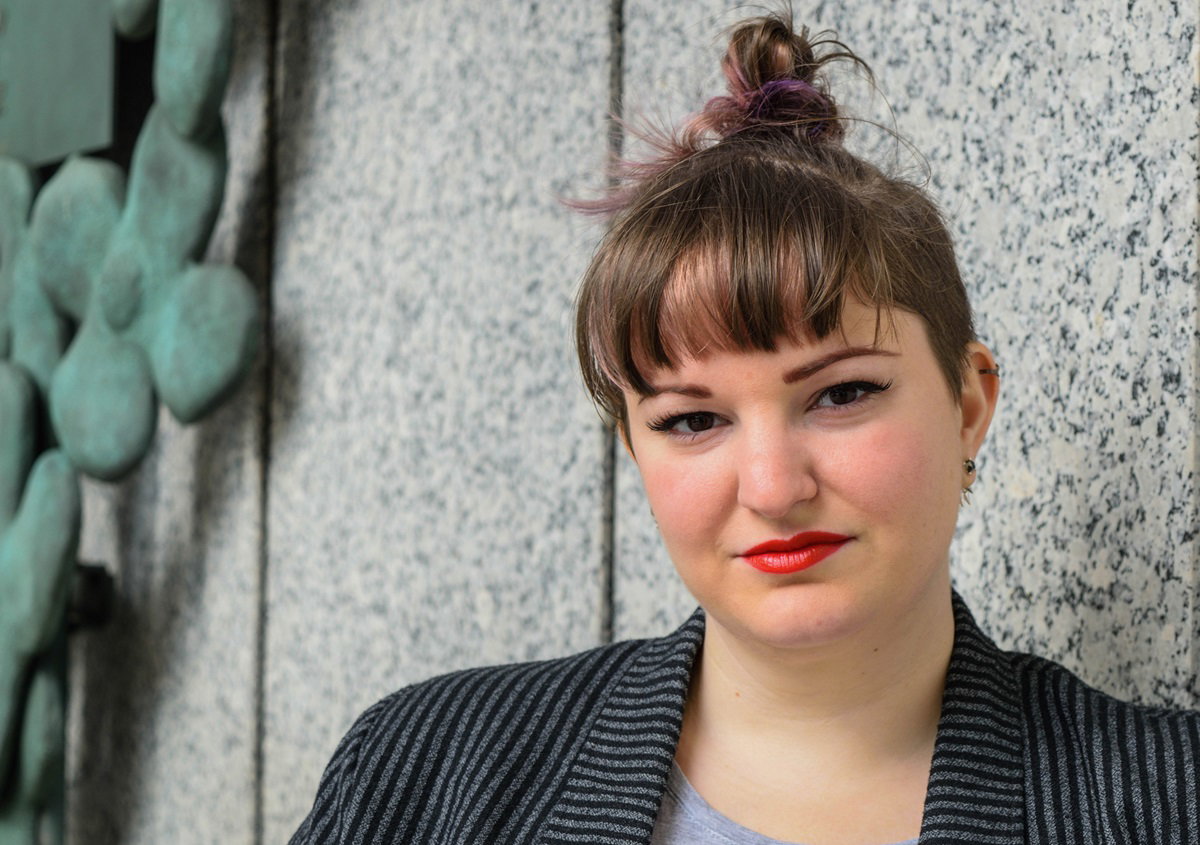 młoda dziewczyna w wieku około 25+ z koczkiem i w marynarce w paski siedzi i patrzy z poważną miną przed siebie