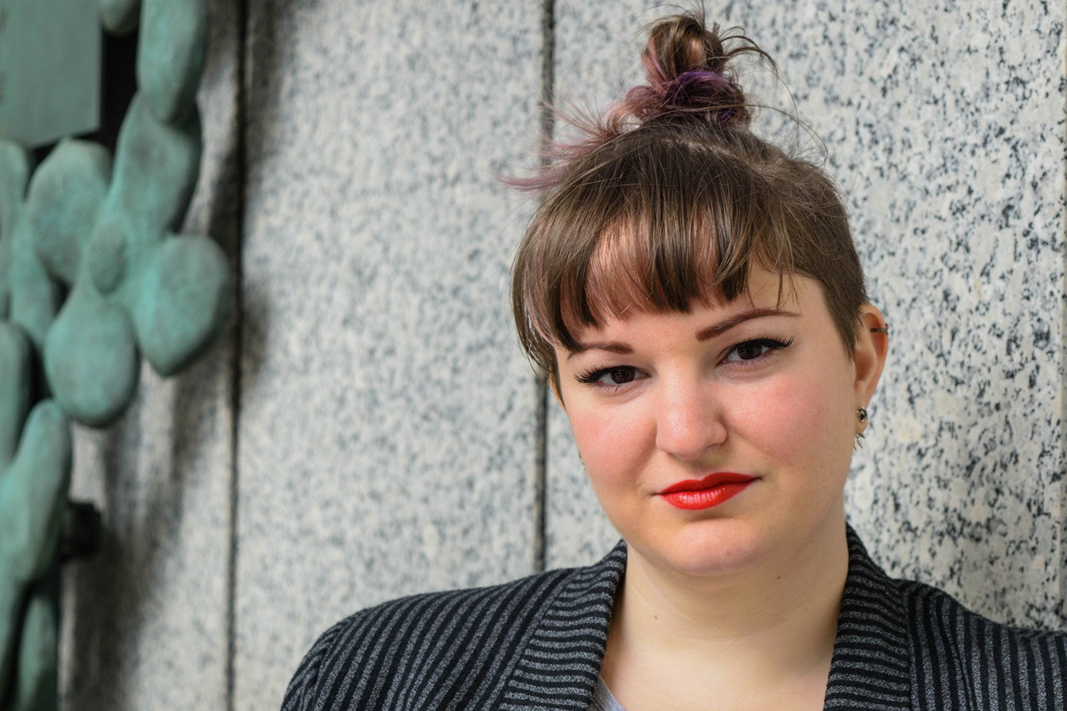 młoda dziewczyna w wieku około 25+ z koczkiem i w marynarce w paski siedzi i patrzy z poważną miną przed siebie