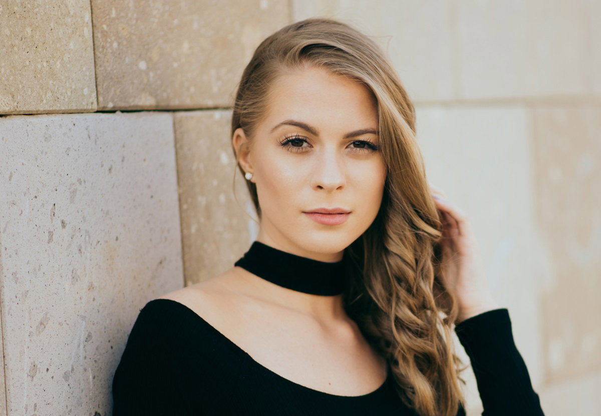 młoda kobieta z długimi pofalowanymi blond włosami i z czarną aksamitka na szyi patrzy rozmarzonym wzrokiem