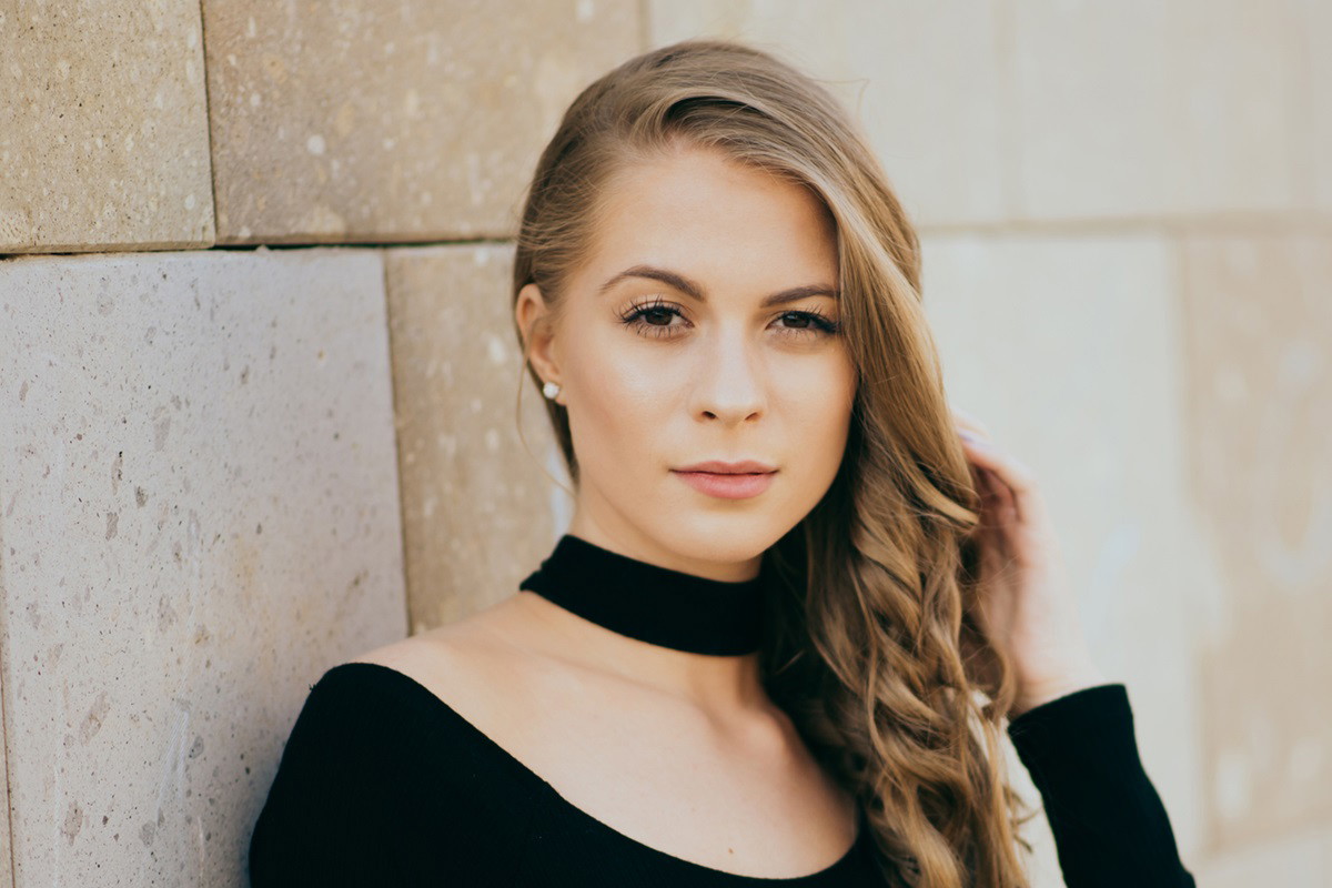 młoda kobieta z długimi pofalowanymi blond włosami i z czarną aksamitka na szyi patrzy rozmarzonym wzrokiem