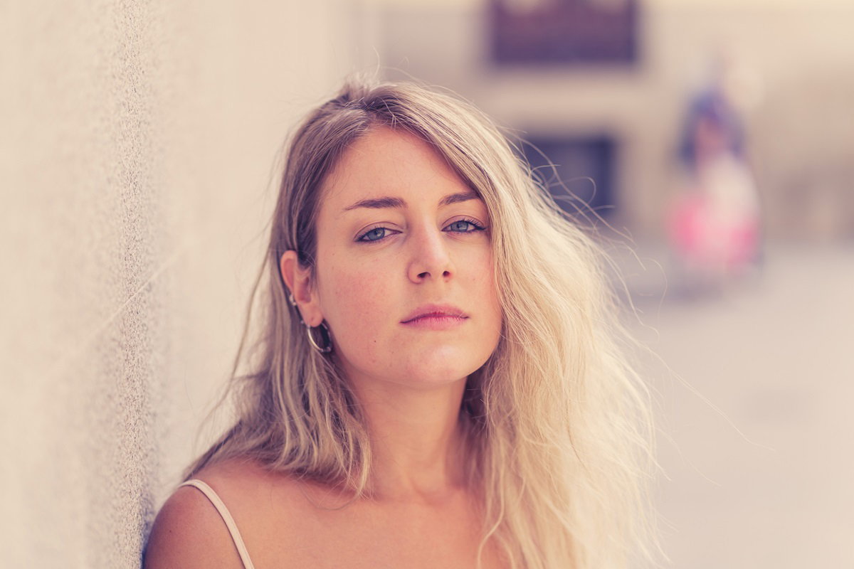 młoda kobieta w wieku około 30 lat z długimi blond włosami stoi smutna pod ścianą na ulicy