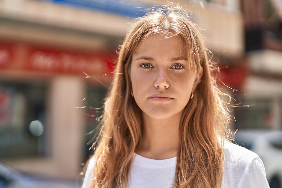 młoda dziewczyna w wieku 20 plus z długimi włosami stoi na ulicy z gniewną miną