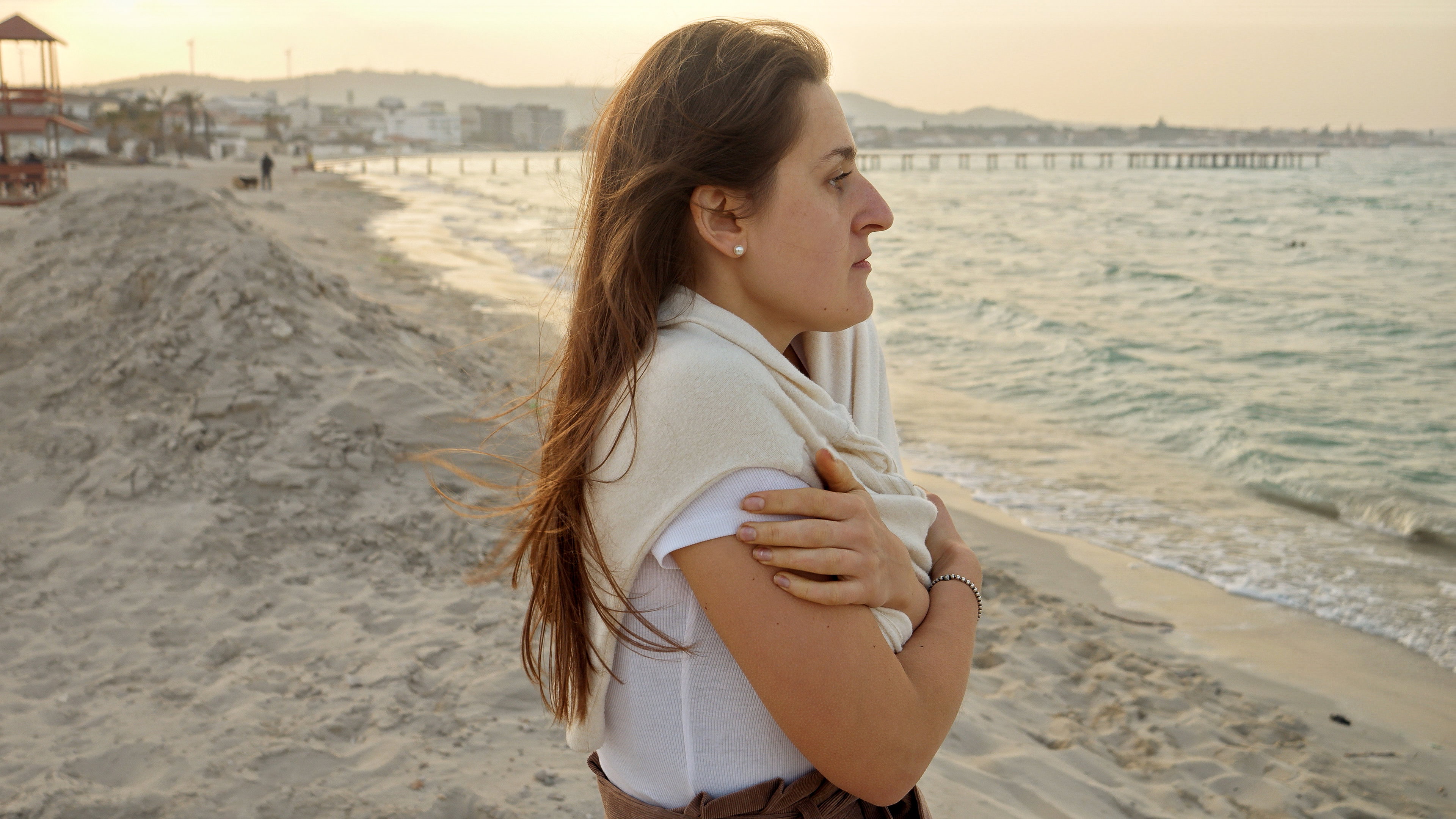 Portrait of young woman with long hair feeling cold on beach at sunset