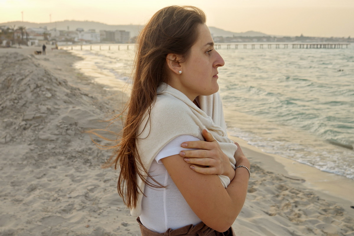 Portrait of young woman with long hair feeling cold on beach at sunset