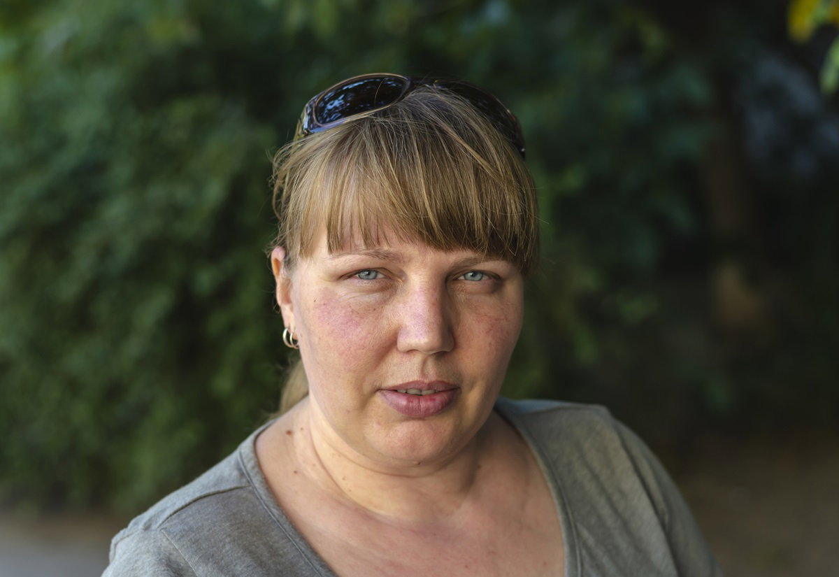 kobieta w wieku około 40 lat z jasnymi włosami z grzywką w szarej bluzce stoi na zewnątrz i patrzy poważnym wzrokiem