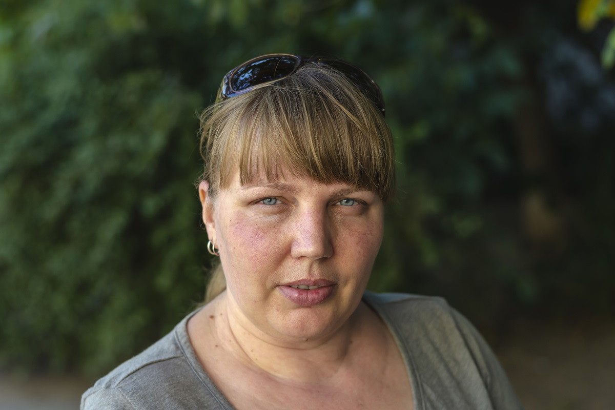 kobieta w wieku około 40 lat z jasnymi włosami z grzywką w szarej bluzce stoi na zewnątrz i patrzy poważnym wzrokiem