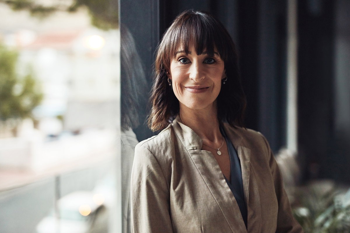 kobieta w wieku około 40 lat z ciemnymi włosami z grzywką stoi na tle ona i uśmiecha się zadowolona