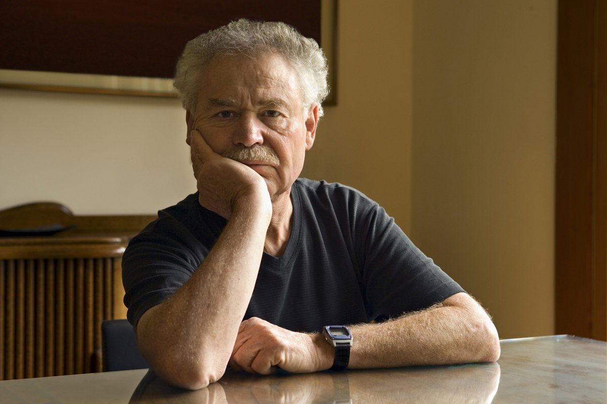 mężczyzna w wieku około 50 lat siwy z wąsami siedzi przy stole i podpiera głowę ręką jest zamyślony i smutny