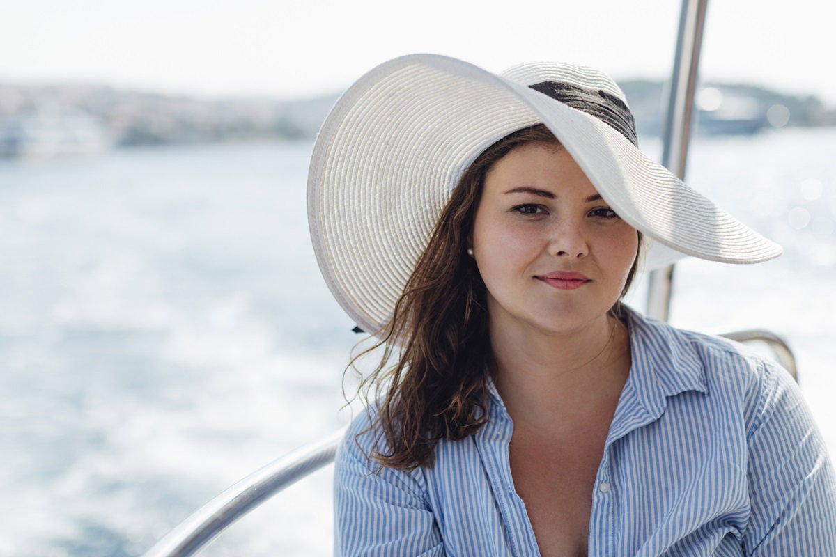piękna kobieta w białym kapeluszu i koszuli w wieku około 30 lat siedzi na pokładzie jachtu i delikatnie się uśmiecha