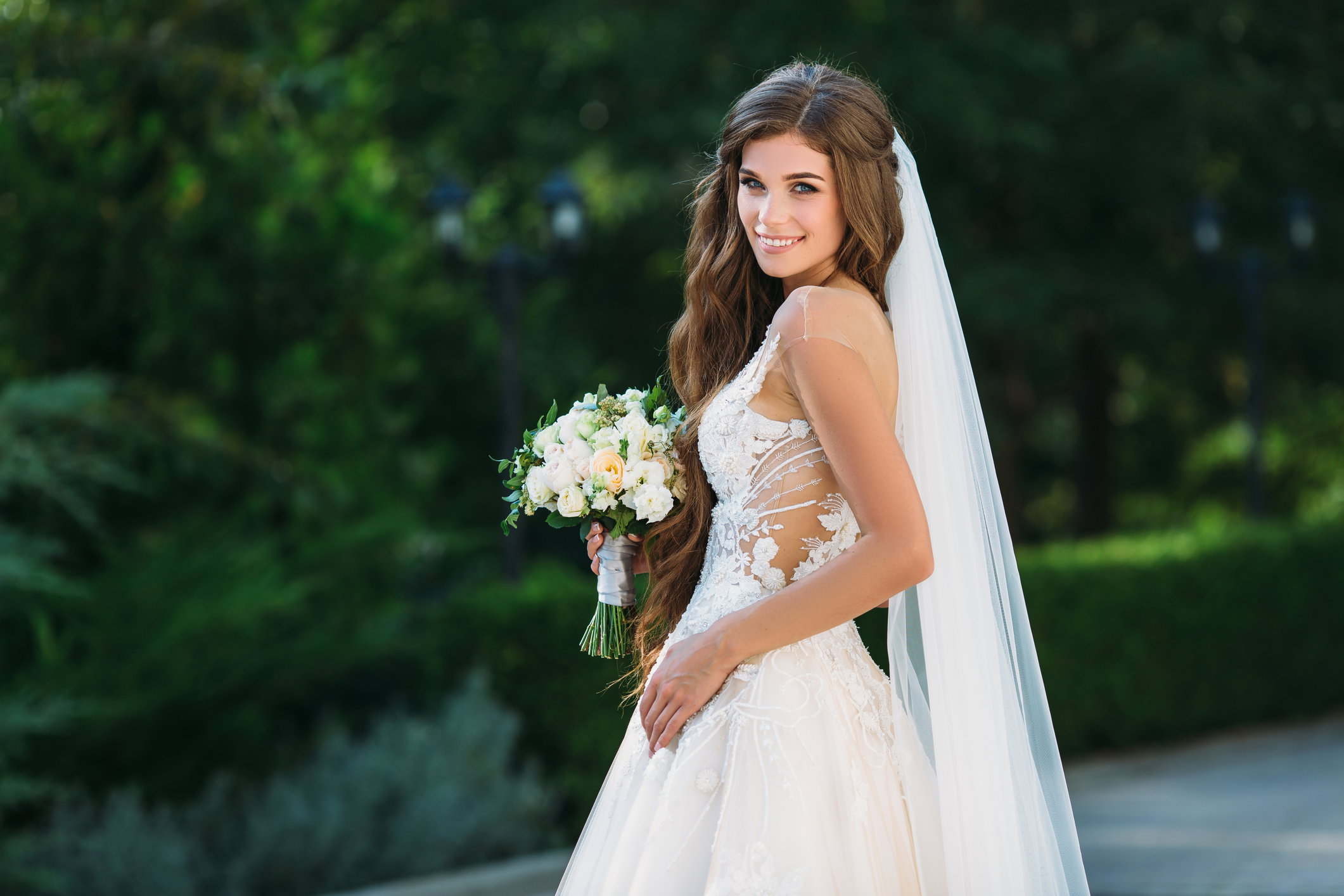 Amazing bride in beautiful white wedding dress hold bouquet of flowers in her hands. Concept of clothes and floristics