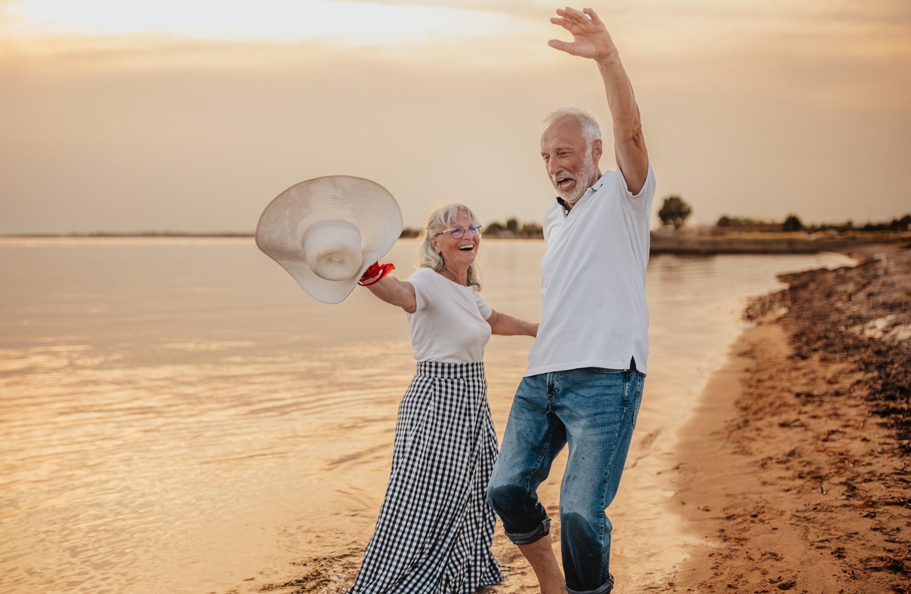Senior couple enjoys a joyful beach vacation while celebrating their love at sunset
