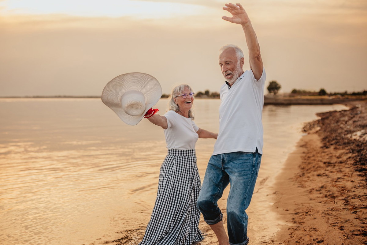 Senior couple enjoys a joyful beach vacation while celebrating their love at sunset
